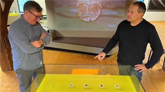 Experten unter sich: Museumsdirektor Dr. Sebastian Möllers (links) und Stadtarchäologe Dr. Andreas Schäfer fachsimpeln über die Fundstücke in der Vitrine. Im Hintergrund läuft das neue Video über die einstige Bedeutung der Schwedenschanze. 