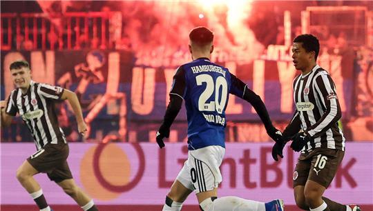 Fábio Vieira (M, Hamburger SV) und Joel Chima Fujita (r, FC St. Pauli) kämpfen um den Ball während Fans vom HSV Pyrotechnik zünden. 