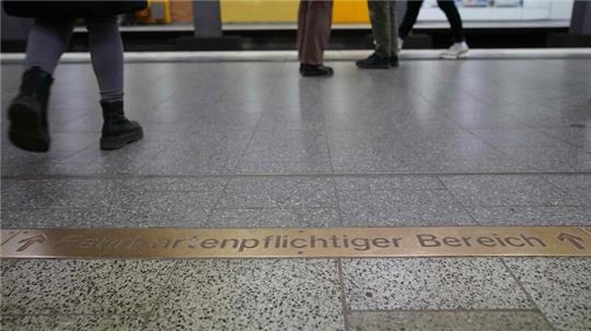 Fahrgäste gehen am Schriftzug „Fahrkartenpflichtiger Bereich“ in einer U-Bahnstation vorbei.