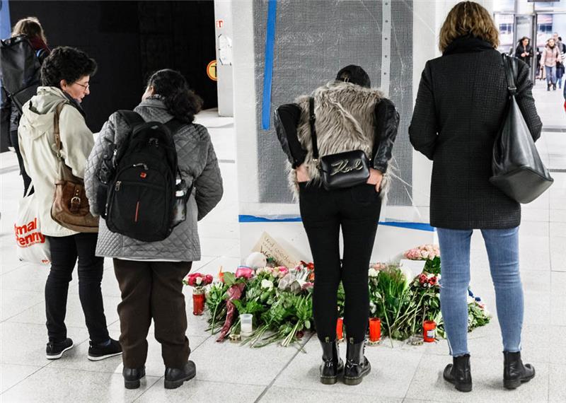 Fahrgäste stehen vor auf dem S-Bahnsteig Jungfernstieg abgelegten Blumen. Foto: Scholz/dpa