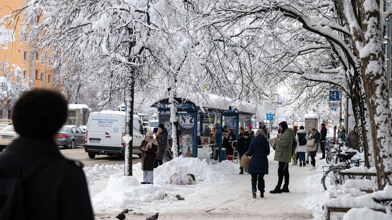 Winterwetter führt zu Flughafen-Stillstand in München Fahrgäste warten an einer verschneiten Haltestelle auf einen Bus.