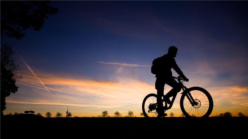 Fahrradfahrer im Morgengrauen: Silhouette vor Sonnenaufgangshimmel in Hannover.