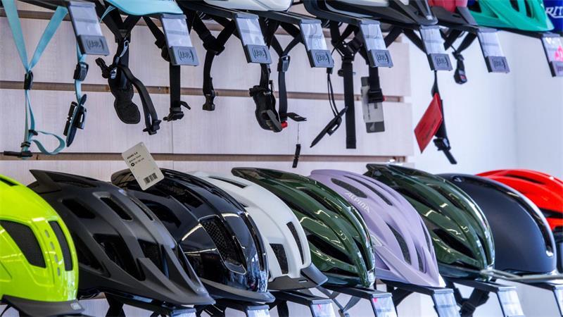 „Risiko für bleibende Schäden“: Chirurg warnt vor E-Scooter-Unfällen Fahrradhelme hängen im Verkaufsraum bei einem Fahrradhändler.