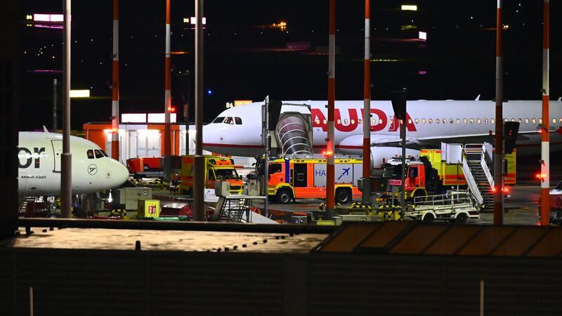 Hamburger Flughafen: Glückliches Ende einer Geiselnahme Fahrzeuge der Feuerwehr und ein Krankenwagen stehen am Flughafen vor einem Flugzeug.