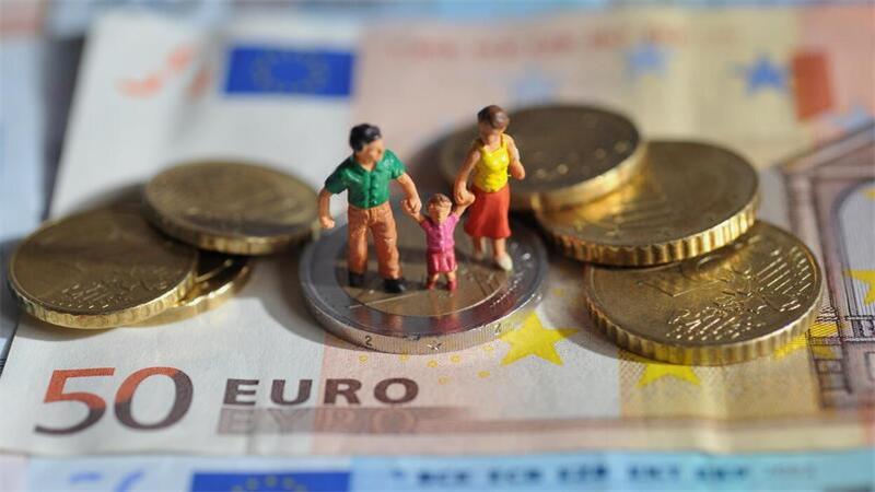 Ein Paar mit einem Kind steht auf einer Zwei-Euro-Münze, die auf Geldscheinen liegt.