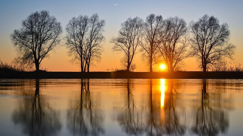 Farbenprächtig leuchtet der Sonnenuntergang über einem gefrorenen See in Brandenburg und spiegelt sich dabei im Eis wieder.