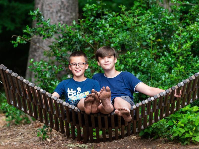 Felix und Niklas Wiede aus Berlin sitzen auf einer Schaukel im Barfußpark in der Lüneburger Heide. Foto: Philipp Schulze/dpa/Archivbild
