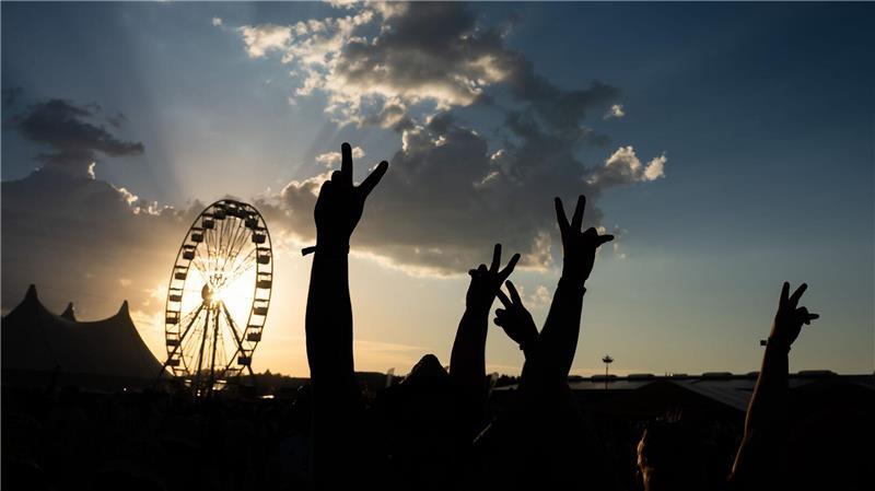 Festivalbesucher halten bei Sonnenuntergang ihre Hände auf dem Southside in die Höhe und sind dabei als Silhouette zu sehen.