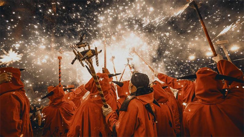 Feuerläufer entzünden beim traditionellen „Correfoc“ bei der Festa Major de Gracia ihre Feuerwerksstäbe unter einem Funkenregen .