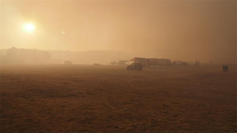Feuerwehrfahrzeuge werden an einem Sammelpunkt vom Qualm eines Waldbrandes in der Nähe des Ortsteils Großhau in der Gemeinde Hürtgenwald eingehüllt.