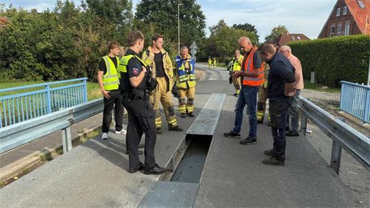 Feuerwehrleute, Polizisten und Mitarbeiter der Kommunalen Betriebe Stade blicken auf das Loch in der Brücke über den Bützflether Kanal.