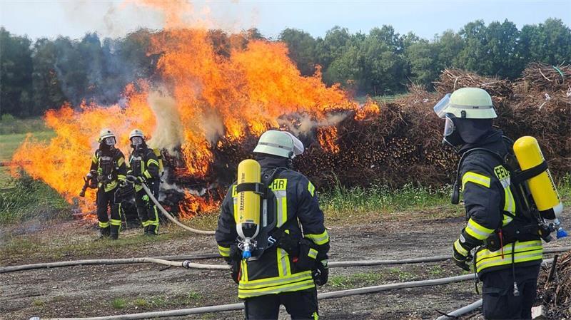 Feuerwehrleute löschen brennende Stackbuschballen auf einem Lagerplatz an der Fährstraße in Hemmoor-Basbeck. Es ist bereits das zweite Großfeuer dort innerhalb von fünf Wochen.