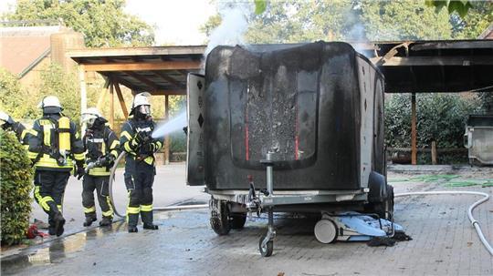 Feuerwehrleute löschen den brennenden Anhänger.