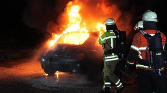 Feuerwehrleute löschen ein brennendes Auto.