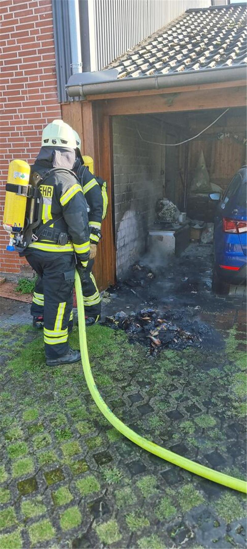 Feuerwehrleute löschen eine brennende Mülltonne in einem Carport in Sauensiek.