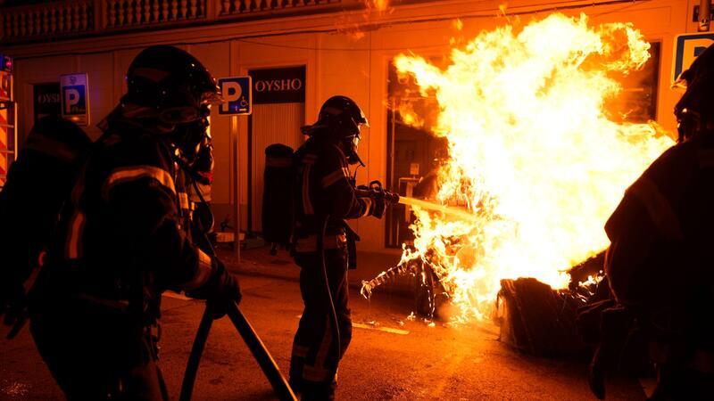 Feuerwehrleute müssen einen von Demonstranten angezündeten Müllcontainer löschen.