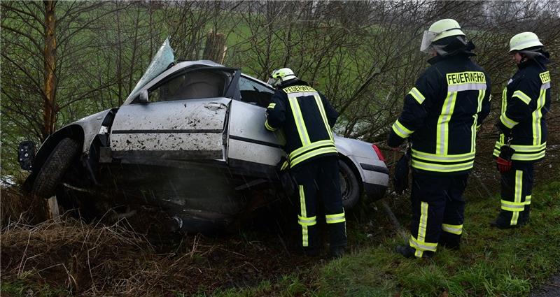 Feuerwehrleute nehmen das Unfallfahrzeug in Augenschein. Der VW-Passat hat sich um den Baum gewickelt und ist total zerstört. Fotos: Beneke
