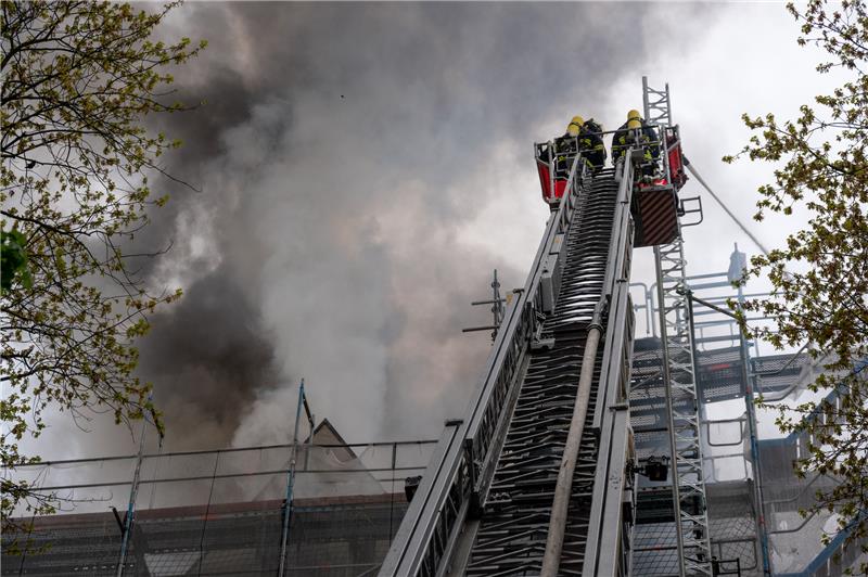 Feuerwehrleute stehen im Korb einer Drehleiter vor dem stark qualmenden Dachstuhl eines Hauses. Beim dem Brand ist ein Mensch verletzt worden. Foto: Jonas Walzberg/dpa