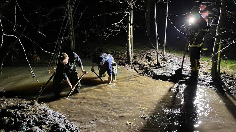 Feuerwehrleute von der Este beseitigen einen Damm in einem Graben, damit das Wasser besser abgepumpt werden kann.