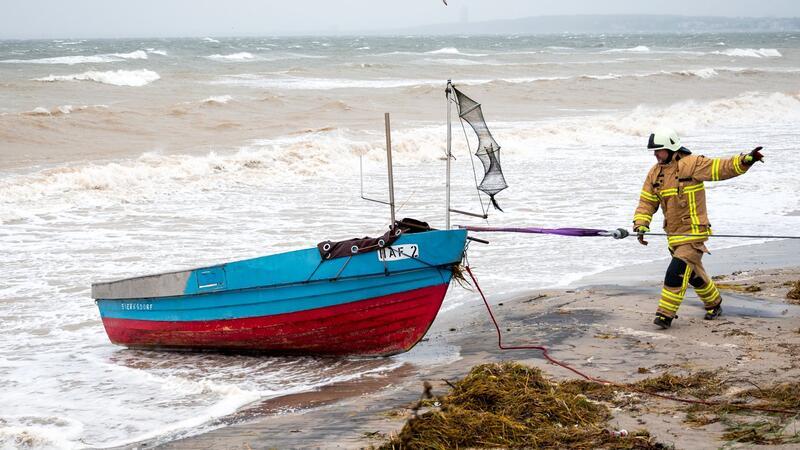 Feuerwehrleute ziehen ein Fischerboot, das vom Wasserstand der Ostsee bedroht wird, vom Strand.