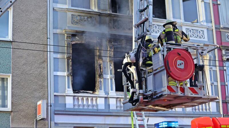 Solingen: Familie mit zwei Kindern stirbt bei Brand Feuerwehrmänner stehen vor dem Mehrfamilienhaus in Solingen; Rauch dringt aus einem der Fenster.