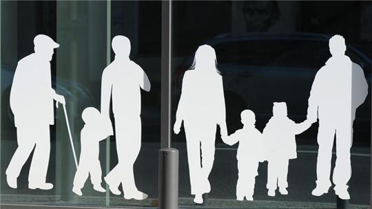 Figuren von Menschen in verschiedenem Alter sind auf Fensterscheiben aufgeklebt.