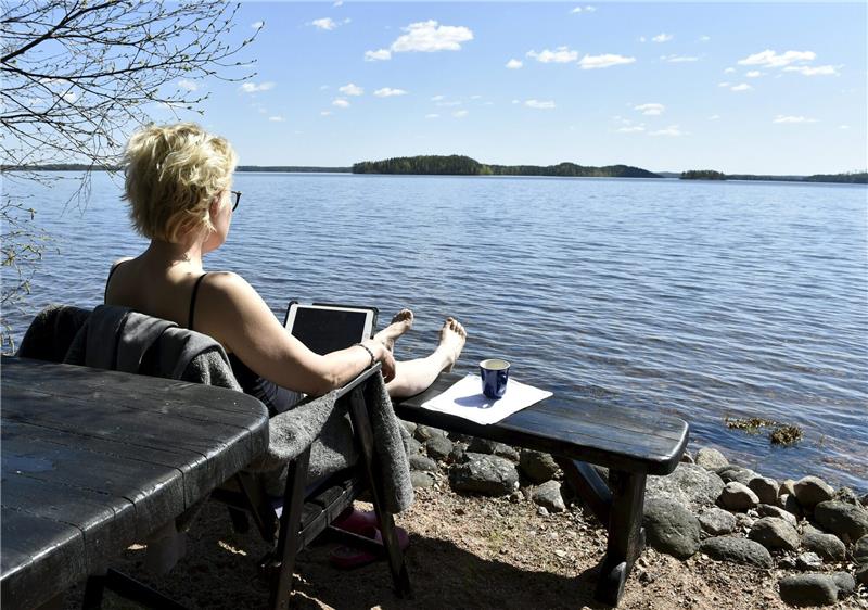 Finnland, Kouvola: Eine Frau arbeitet am Ufer des Sees Vuohijärvi. Während der Corona-Pandemie wanderten viele Beschäftigten ins Home-Office. Aber mobil im Ausland arbeiten? Deutschlands große Unternehmen handhaben das ganz unterschiedlich. Foto: Jussi Nukari/Lehtikuva/dpa