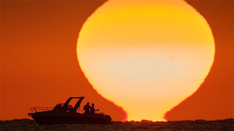 Fischer zeichnen sich als Silhouetten auf einem Boot ab, während die Sonne im Libanon über dem Mittelmeer untergeht.
