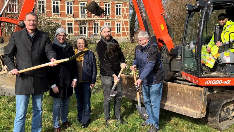 Flecken-Bürgermeister Jörk Philippsen beim Burginsel-Spatenstich mit Knut Willenbockel, Gunda Kiefaber, Julian Benesch und Jürgen Philipp. Rechts im Jacobs-Bagger sitzt Markus Will (von links). Im Hintergrund ist das Horneburger Schloss zu sehen.