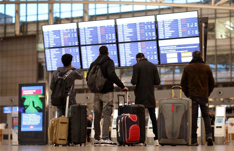 Fluggäste stehen vor einer Anzeigetafel im Terminal 1 des Flughafens. Foto: Christian Charisius/dpa