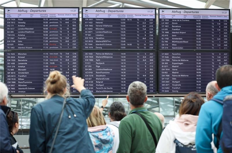 Flugreisende stehen unter den Anzeigetafeln in Terminal 1 am Airport Hamburg. In Hamburg haben die Sommerferien begonnen. Foto: Christian Charisius/dpa