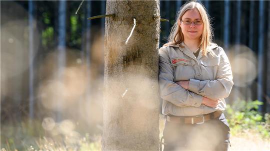 Försterin Katharina Rekowski lehnt an einem Baumstamm im Wald. Der Anteil von Frauen in Forstberufen ist in den vergangenen Jahren kontinuierlich gestiegen.