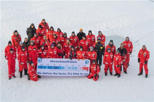 Forscher des Alfred Wegener Instituts mit einem Transparent mit der Aufschrift "#Scientists4Future - We deliver the facts. It's time to act" in der Arktis.