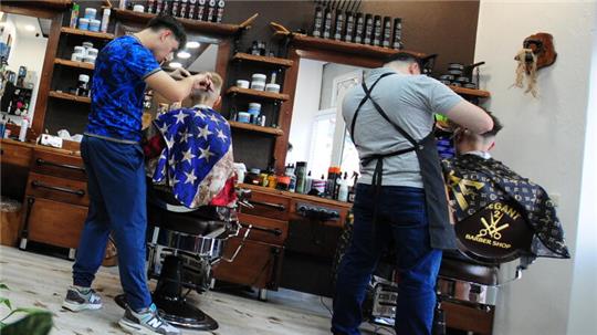 Ein Junge und ein Mann lassen sich in einem Barbershop die Haare schneiden.