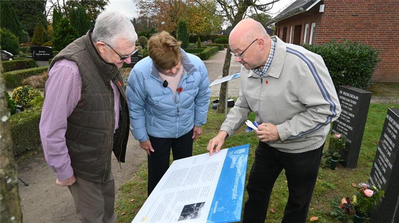 Frank Hoferichter mit Rose und Chris Askew an der Infotafel auf dem Friedhof in Kutenholz.