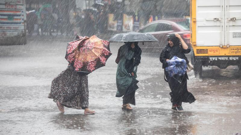 Frauen gehen bei Regen über eine Straße in Bangladesch.