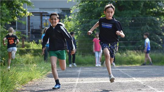 Zwei Viertklässler laufen auf einer Laufbahn nebeneinander.