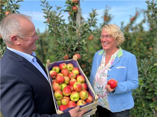 Freude über schmackhafte Früchte: Claus Schliecker von der Fachgruppe Obstbau überreicht Ministerin Barbara Otte-Kinast (CDU) bei der Apfelsaisoneröffnung in Guderhandviertel eine Kiste mit dem Frühapfel Sweetango, im Hintergrund reift in d