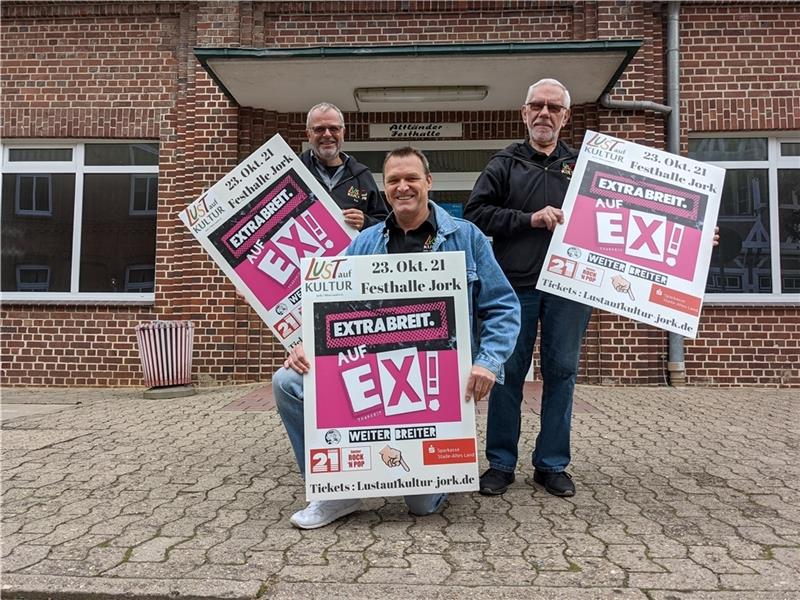 Freuen sich, dass über die 2G-Regel mehr Besucher beim Extrabreit-Konzert erlaubt sind: Frank Deppe, Matthias Gerth und Herbert Scharf (von links) mit Plakaten vor der Festhalle Jork. Foto: Battmer