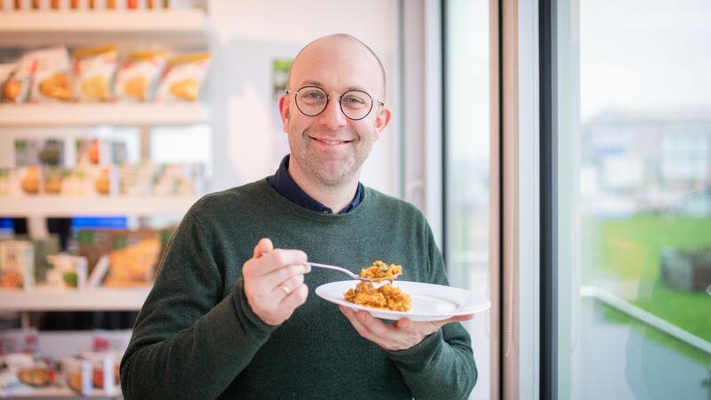 Frosta-Marketingleiter Sebastian Bernbacher verkostet das neue Produkt "Butter Chicken", ein Hähnchen-Reis-Gericht.
