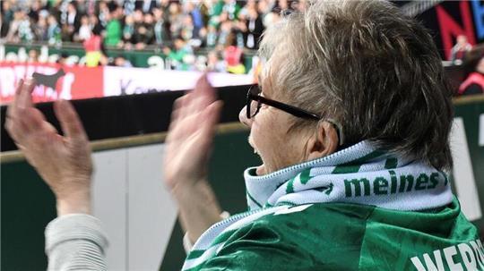 Eine ältere Frau im Stadion klatscht in die Hände.