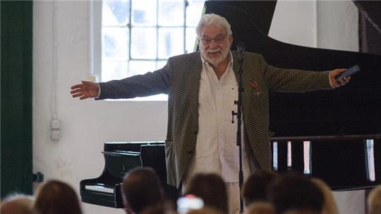 Dieter Klar steht mit ausgebreiteten Armen auf der Bühne vom Schloss Agathenburg und freut sich über die hohe Auszeichnung mit dem Bundesverdienstkreuz