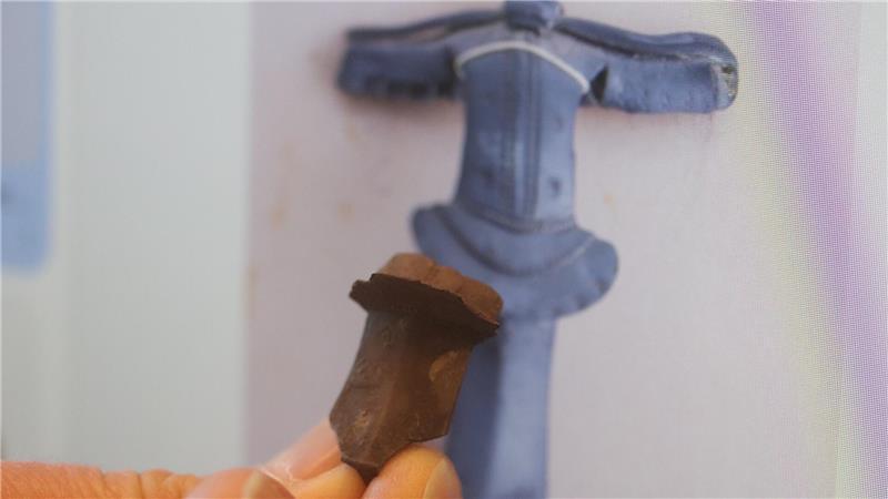 Fundstück: Teil einer Rollenkappenfibel aus dem 1. Jahrhundert. Im Hintergrund die Abbildung einer vollständigen Fibel.