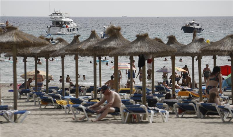 Gäste liegen am Strand von Paguera auf Mallorca oder gehen schwimmen. Foto: Clara Margais/dpa