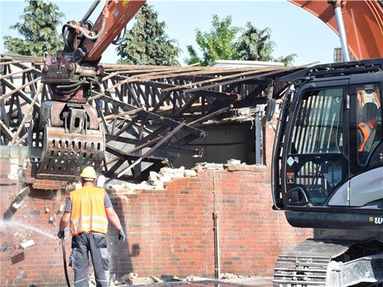 Ganze Arbeit: Der Abbruchbagger beißt sich durch Holz und Mauer. Um die Staubentwicklung einzudämmen, wird die Szene mit Wasser besprüht.