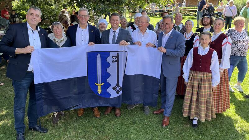 Gemeinsam halten Deutsche und Letten die Flagge von Ludza Novads in Händen.