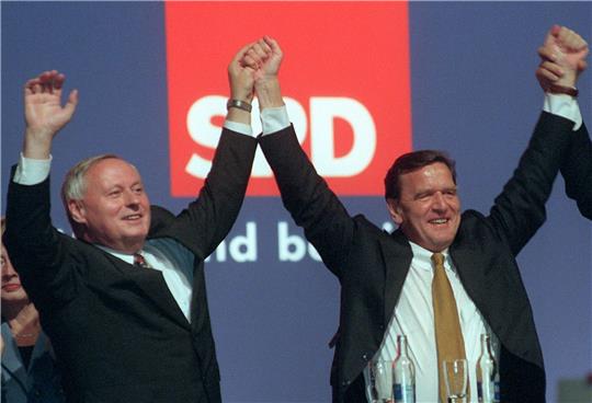 Gerhard Schröder (r) und Oskar Lafontaine halten sich bei einer Veranstaltung an den Händen.
