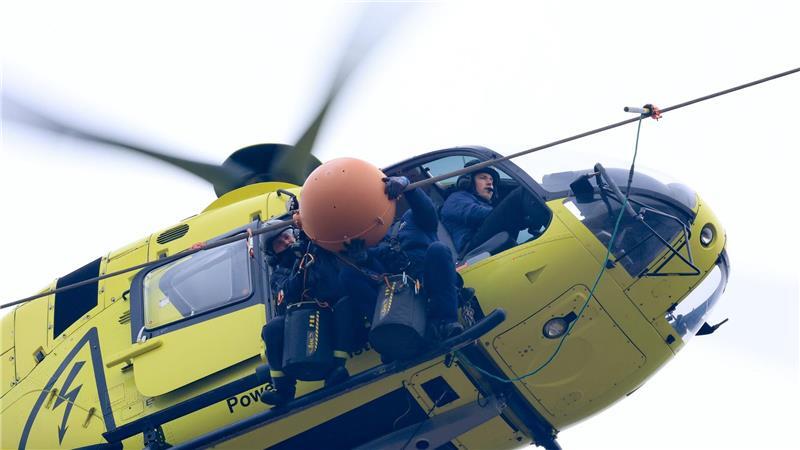 Gesichert mit Gurten sitzen die Monteure auf den Hubschrauberkufen während der Arbeiten.