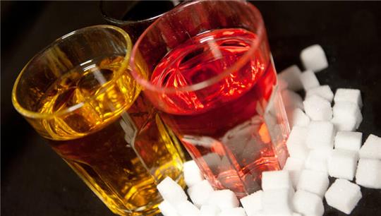 Gläser gefüllt mit roter Limonade, und einem Energy-Drink stehen neben Zuckerwürfeln auf einem Tisch.