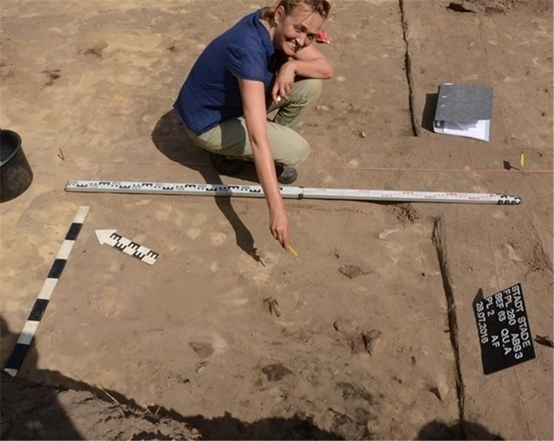 Grabungsleiterin Andrea Finck zeigt auf die dunklen Schatten einer alten Feuerstelle (unten).